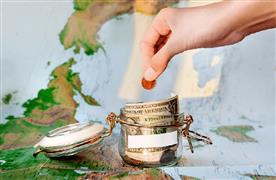 یک دست زنانه درحال انداختن سکه‌ای در یک ظرف شیشه‌ای که مقداری پول در آن است و پس‌زمینه‌اش، نقشه جهان